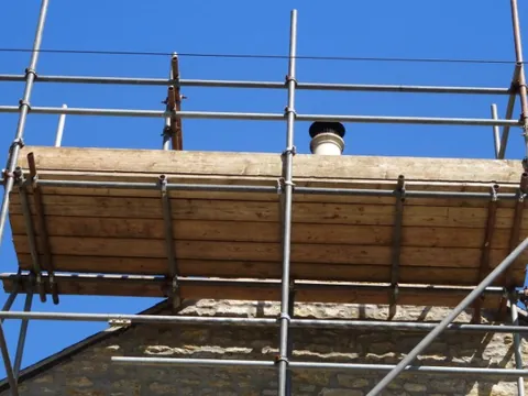 Andamio junto a una chimenea de piedra durante una revisión de cubierta