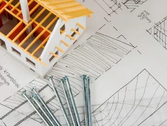 Maqueta de vivienda sobre planos, en referencia a la tramitación de ayudas a la rehabilitación