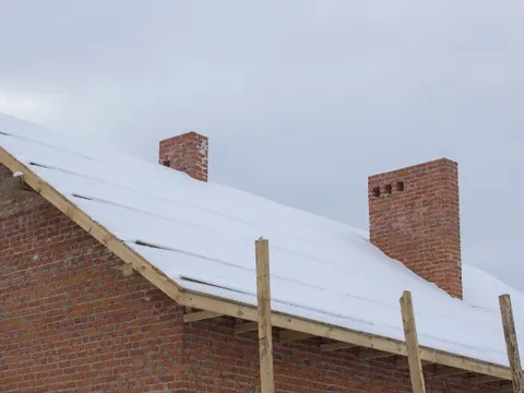 Nieve sobre el tablero de una cubierta en obra, con chimeneas de ladrillo