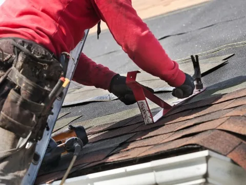 Operario instalando teja asfáltica con martillo sobre un tejado nuevo